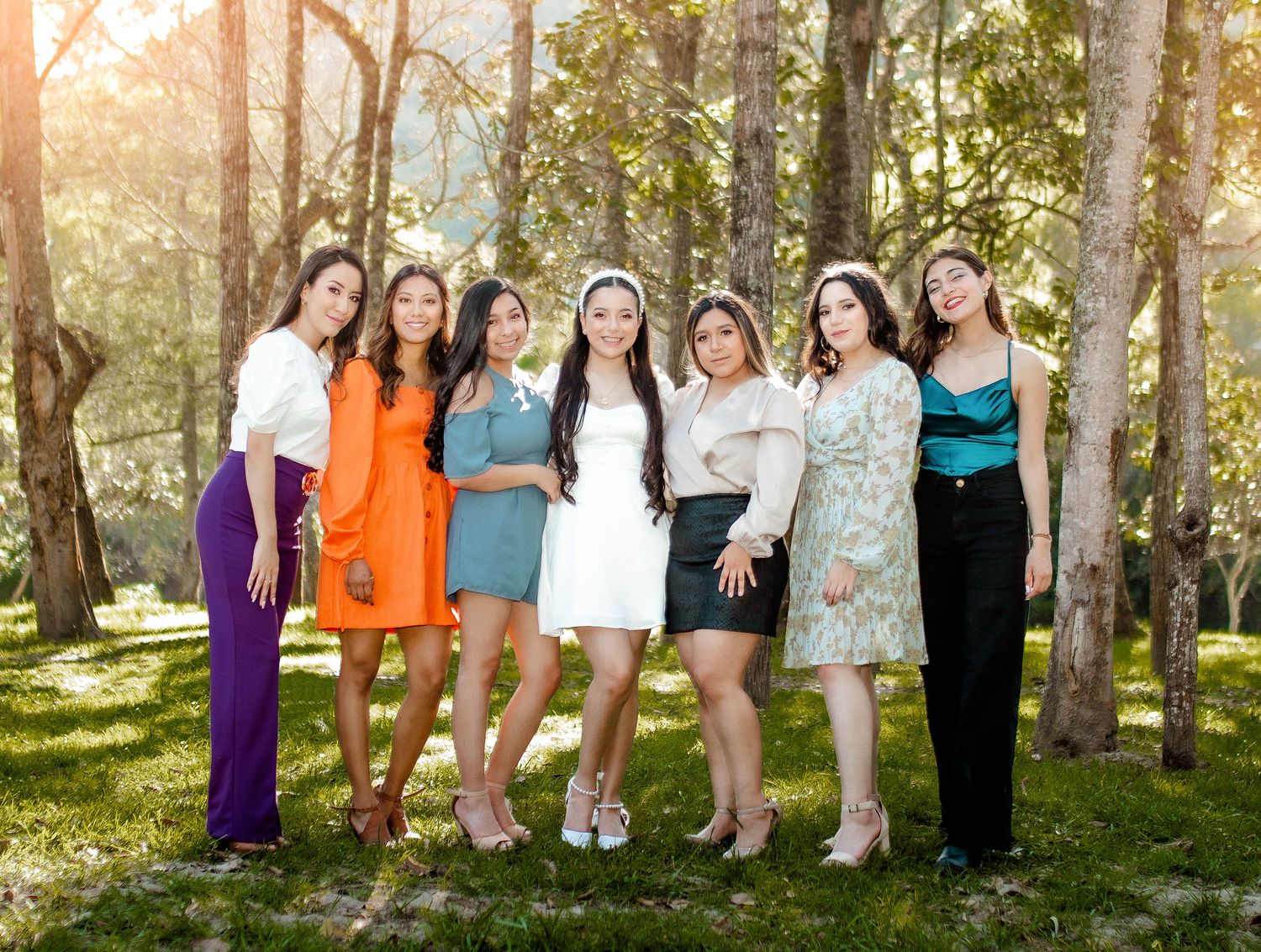 Row of bridesmaids posing casually outdoors among trees.