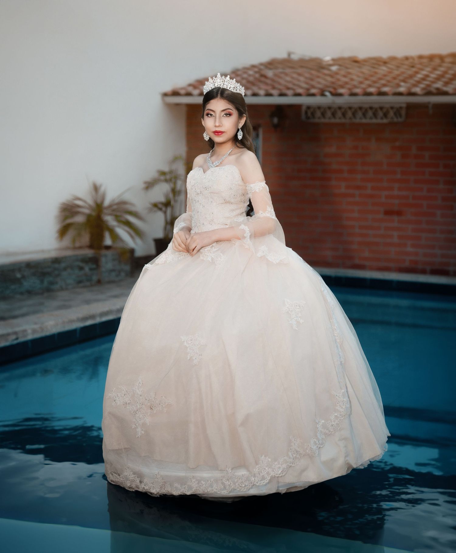 Five connected photos of a person in an elegant white quinceañera dress posing near a blue swimming pool at dusk.