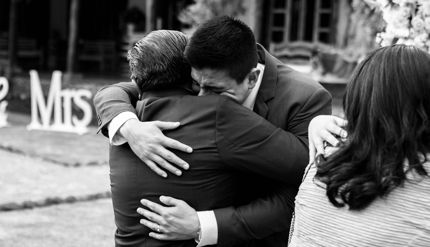 Two people share an emotional embrace at an outdoor event captured in black and white photography.