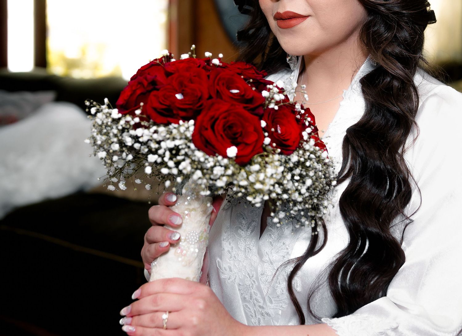 A bridal bouquet of red roses and baby's breath held by someone in a white lace dress.