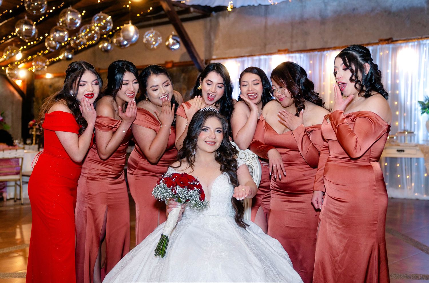 A bride in white surrounded by bridesmaids wearing matching rust-colored dresses.