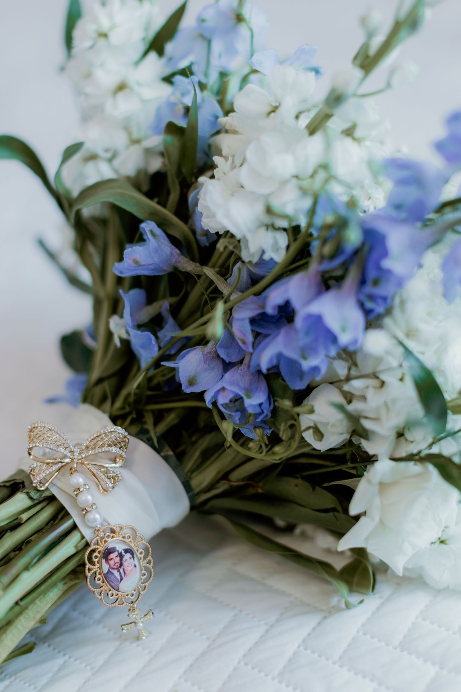 A bridal bouquet of white and blue flowers tied with a white ribbon and decorated with delicate gold bow ornaments.