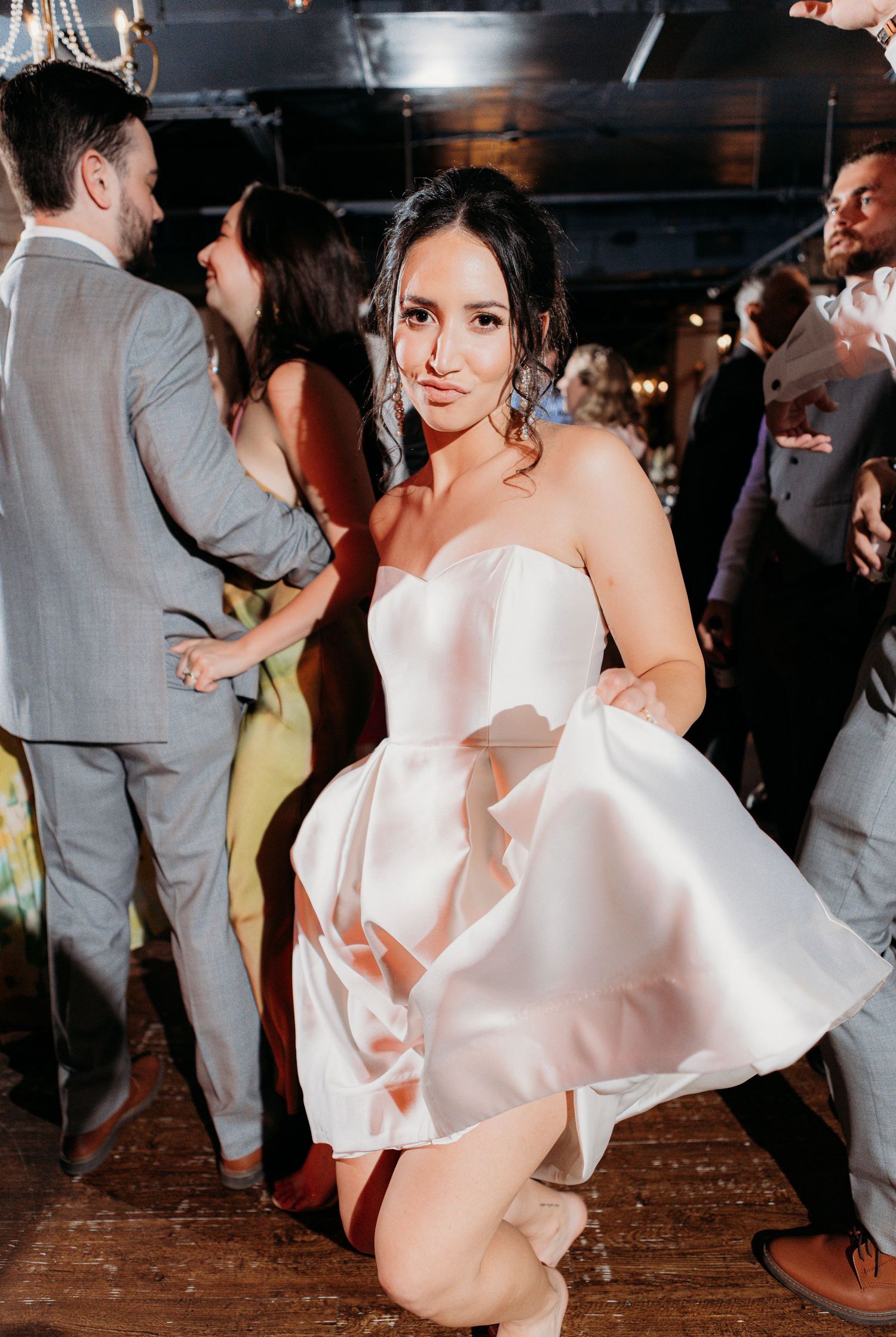 A woman in a short white strapless dress dances on a dark dance floor at a celebration event.