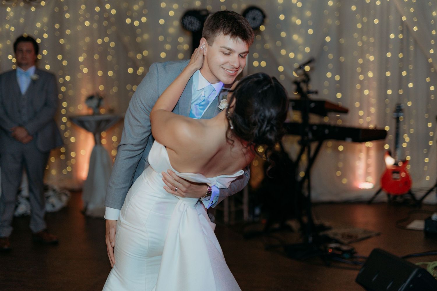 Two people share an intimate dance at a wedding reception with string lights creating a romantic backdrop.