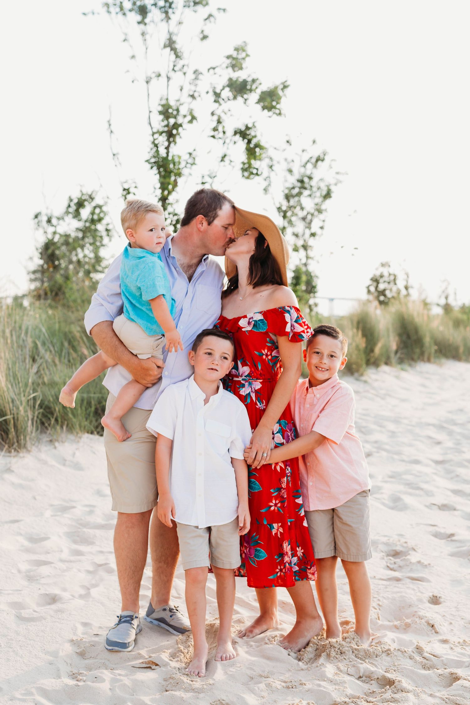 A loving family shares a tender moment together on a sandy beach with green foliage in the background.