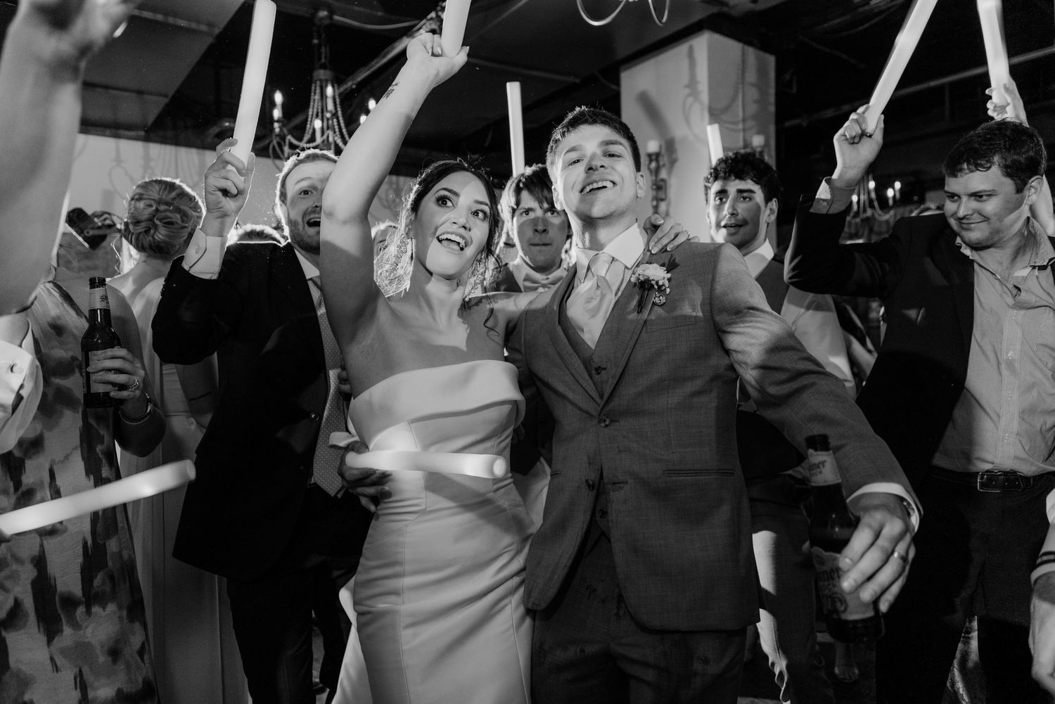 Wedding party celebrates on dance floor under hanging decorations during reception festivities.