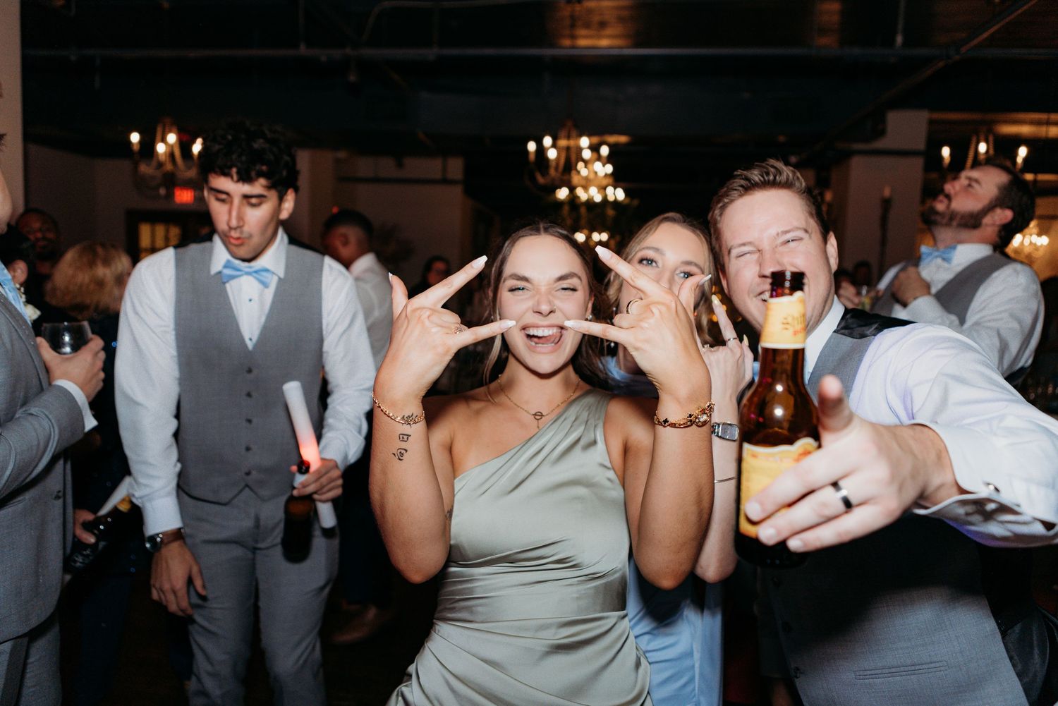 Guest posing with peace signs and holding drink during celebratory wedding reception.