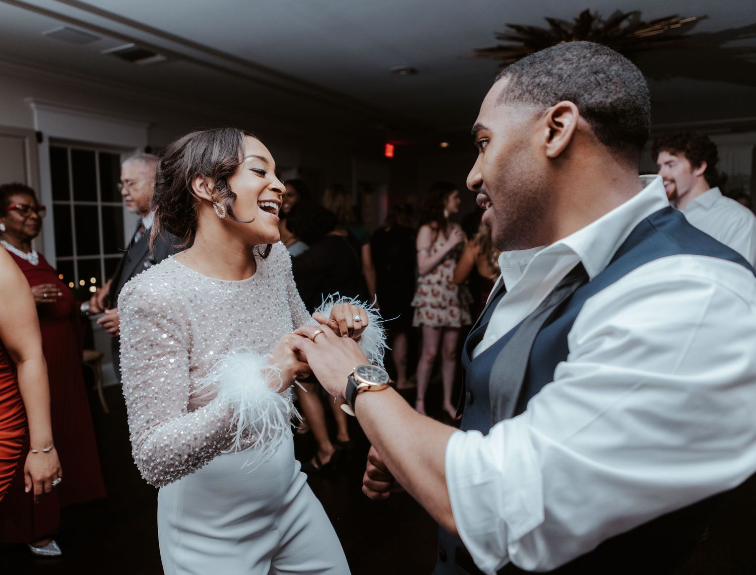 A bride and groom share a joyful moment dancing together at their wedding reception in a dimly lit room.