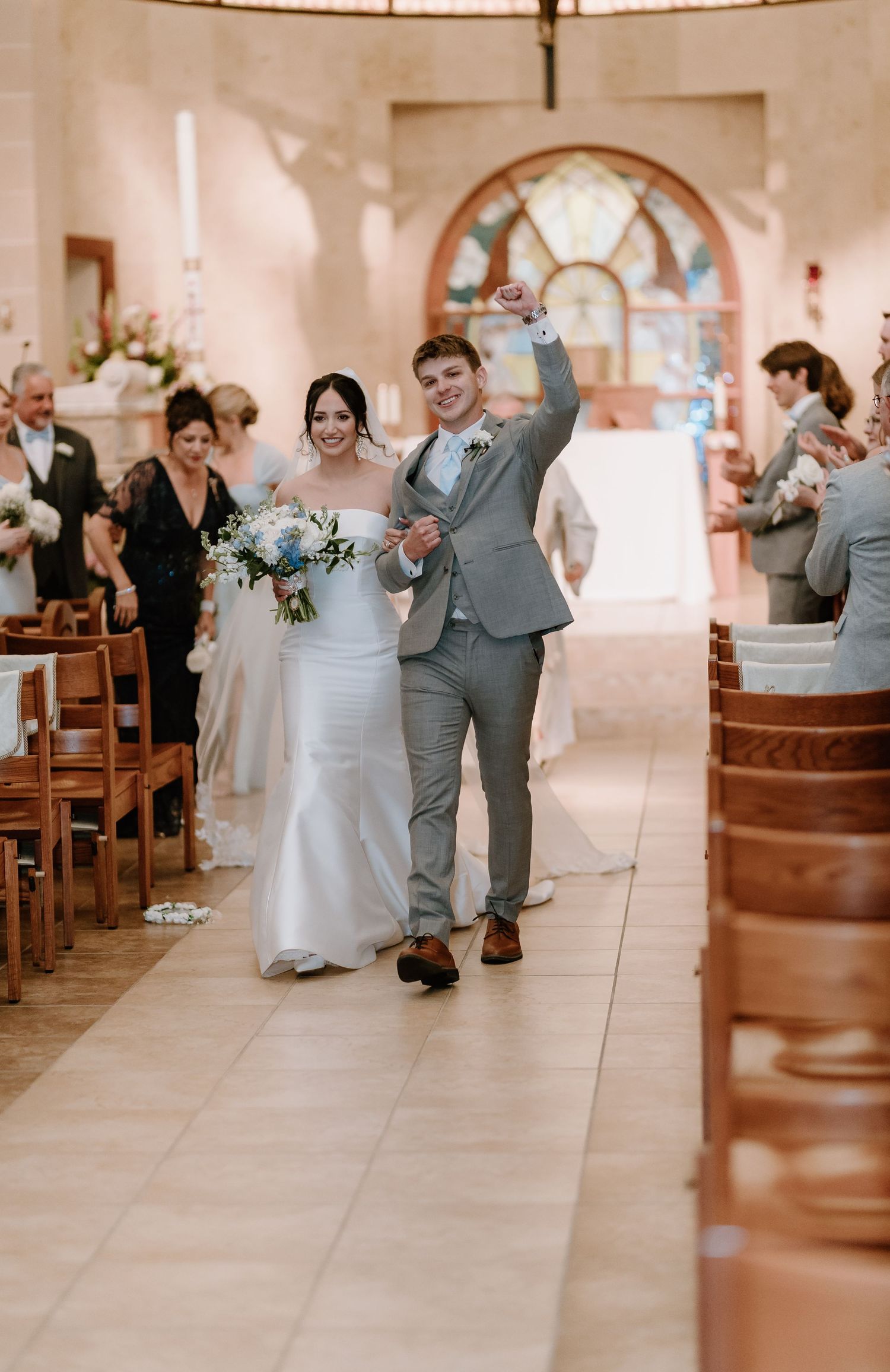 A wedding couple celebrates while walking down the church aisle as guests look on from wooden pews.
