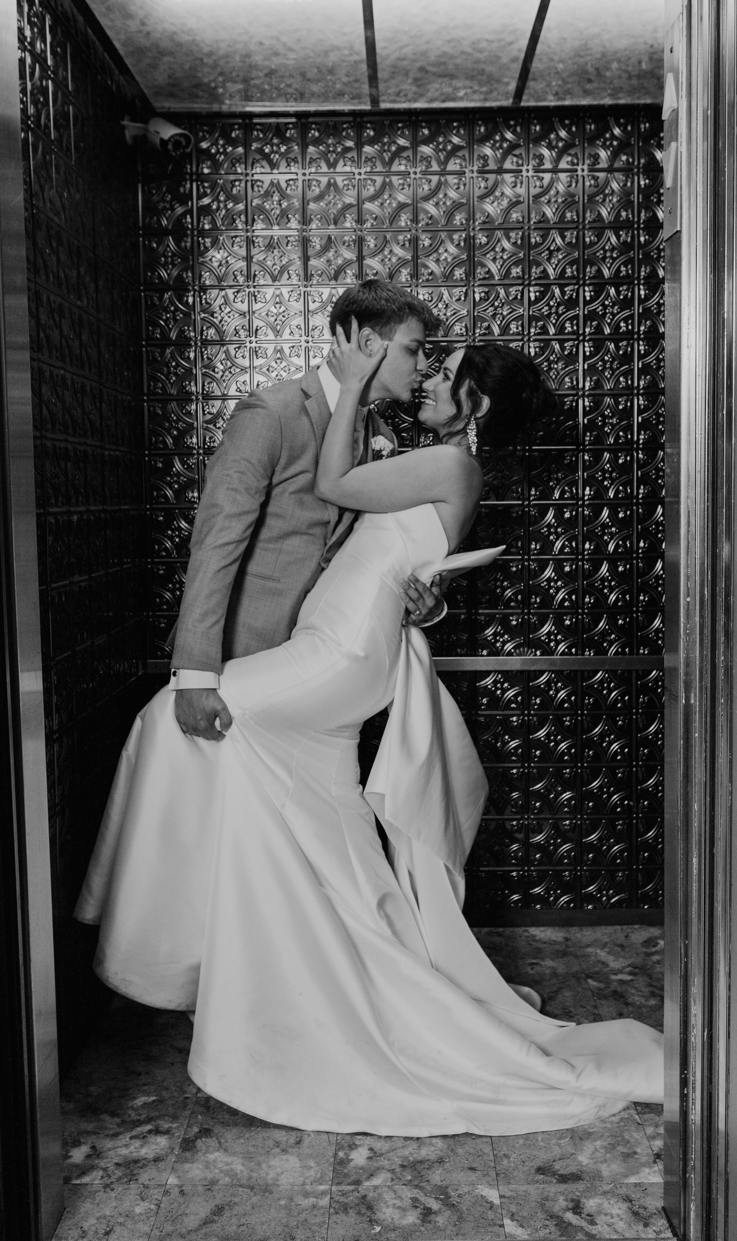 Romantic black and white portrait of newlyweds posing against a decorative metal wall.
