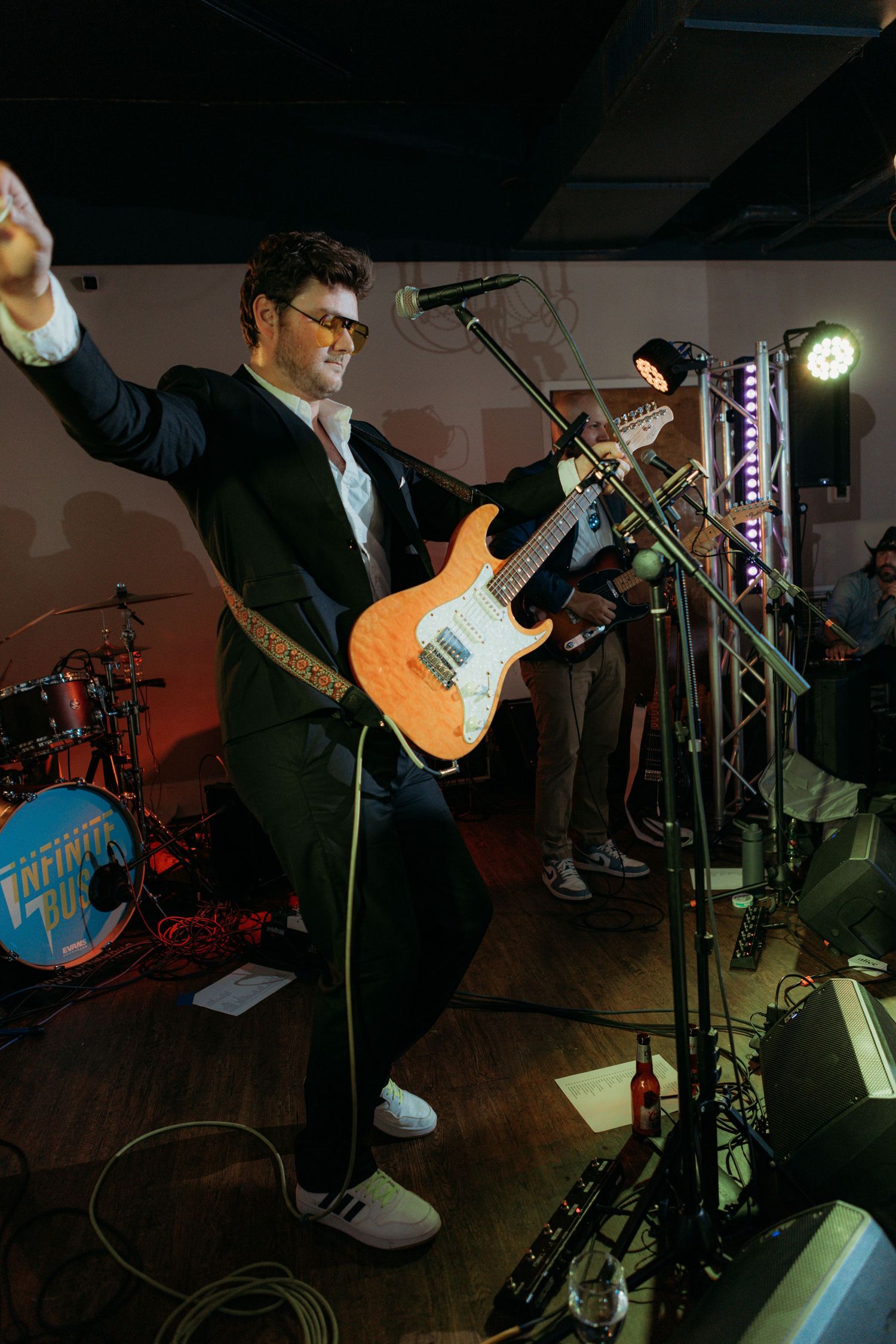 Musician performs energetically with an electric guitar on stage during a live concert with spotlights and equipment.