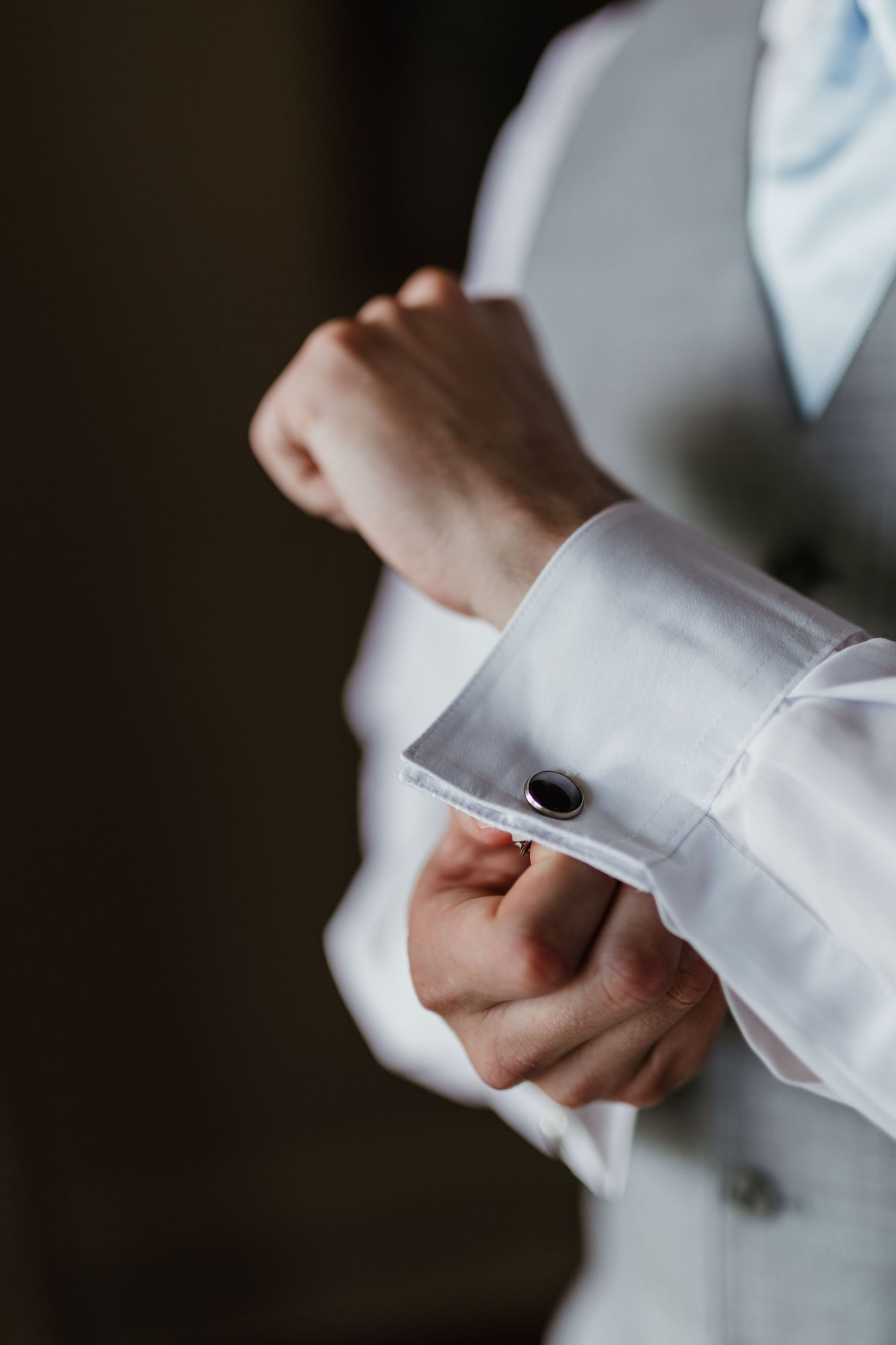 Close-up shot of hands adjusting a white dress shirt cuff with black cufflink in formal attire.