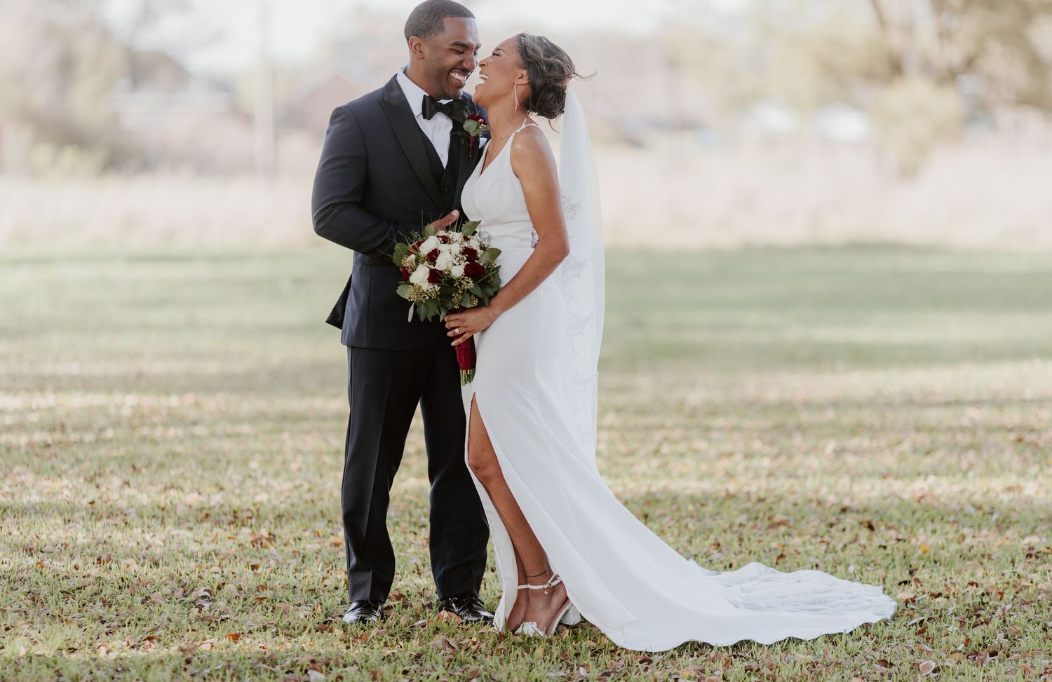 A newlywed couple shares a tender moment outdoors in formal wedding attire with white gown and black tuxedo.