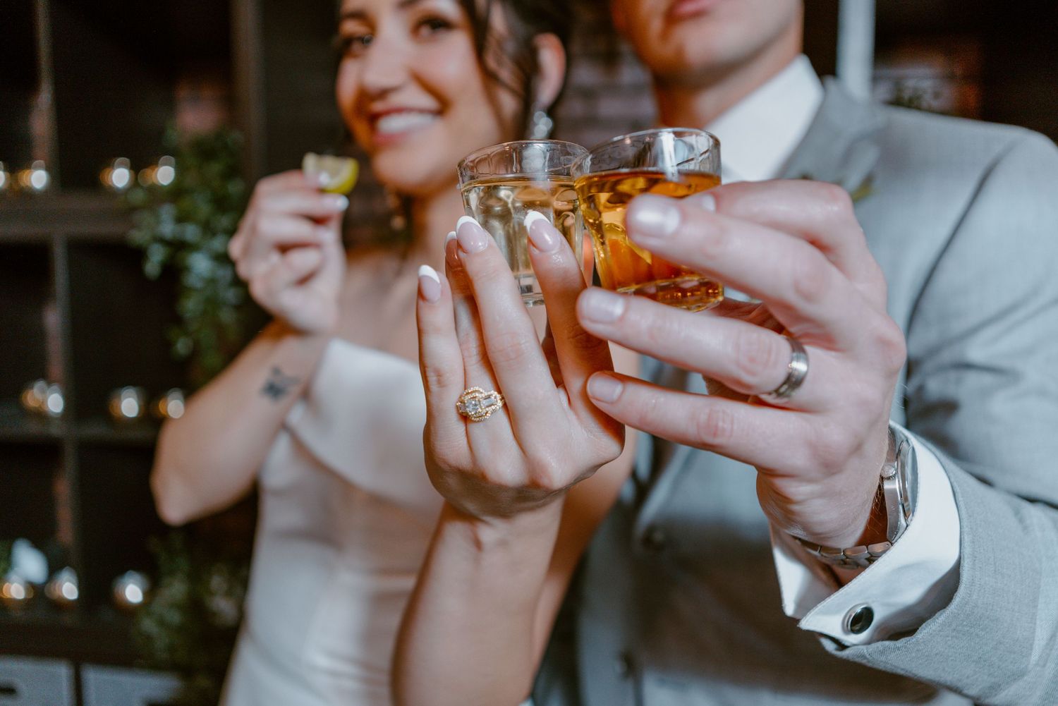 Wedding guests toasting with drinks while wearing elegant attire at a dimly lit reception.