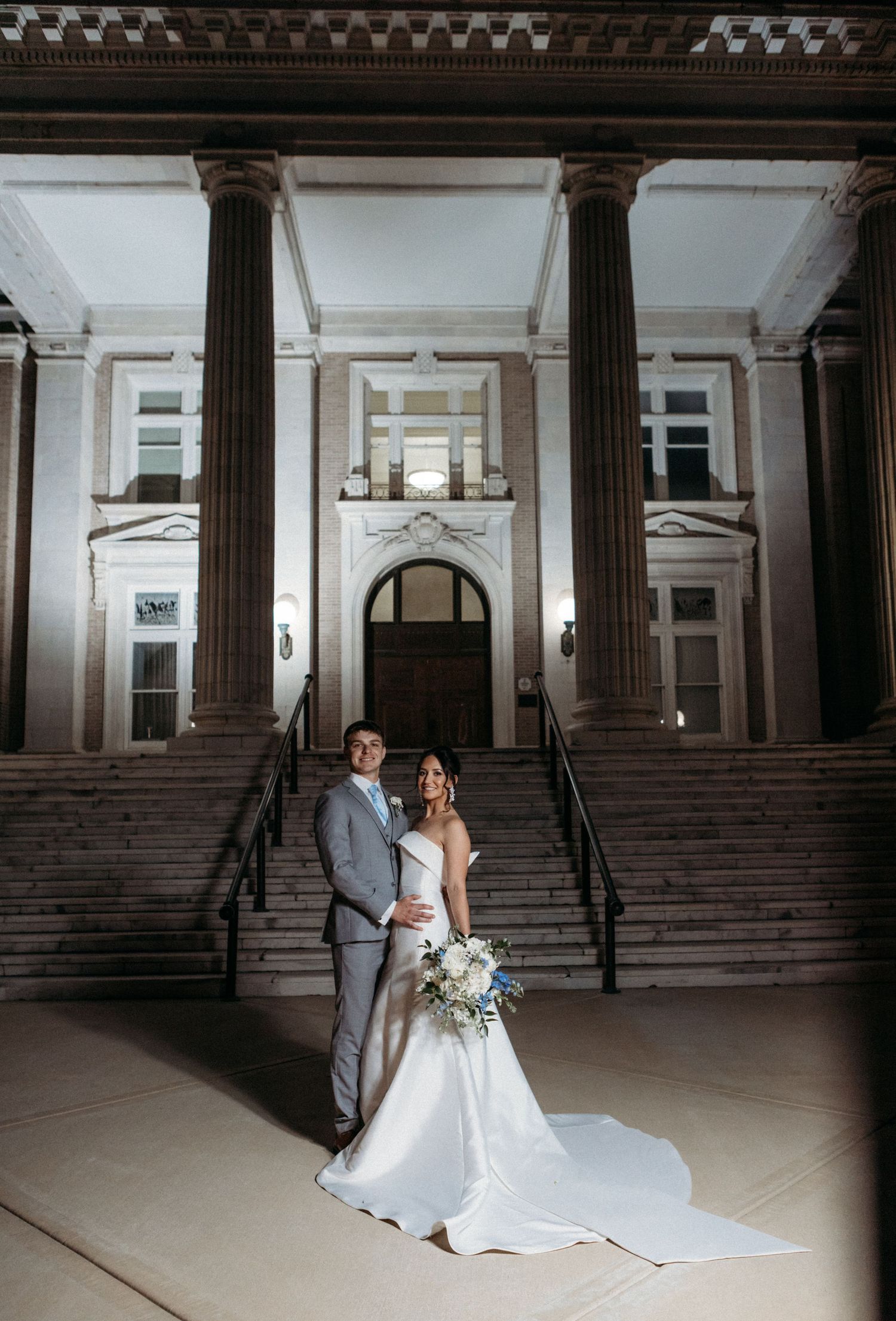Classic neoclassical building entrance with grand columns and stairs providing an elegant backdrop for a wedding couple.