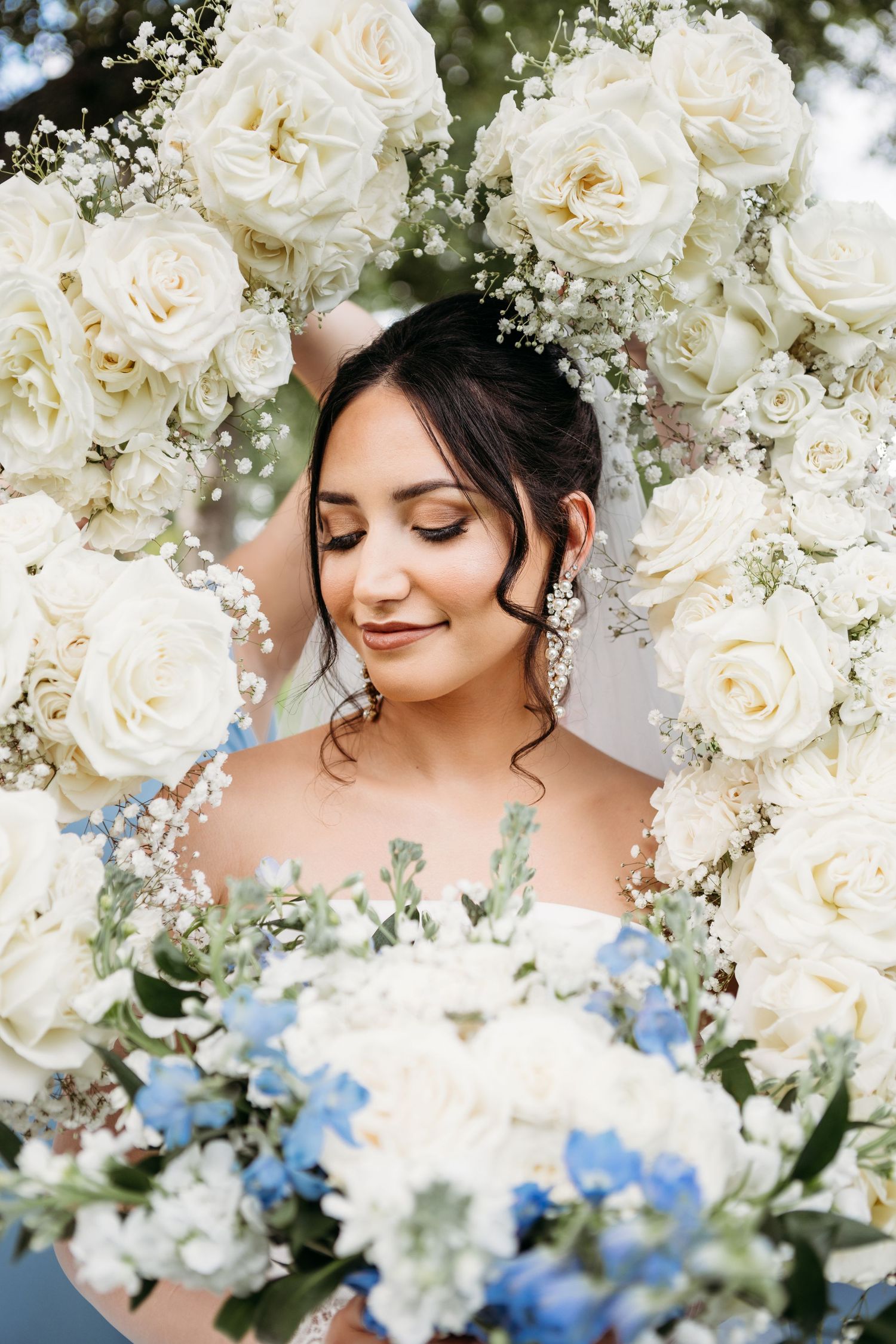 Romantic bridal portrait surrounded by white roses and delicate blue flowers with baby's breath floral accents.