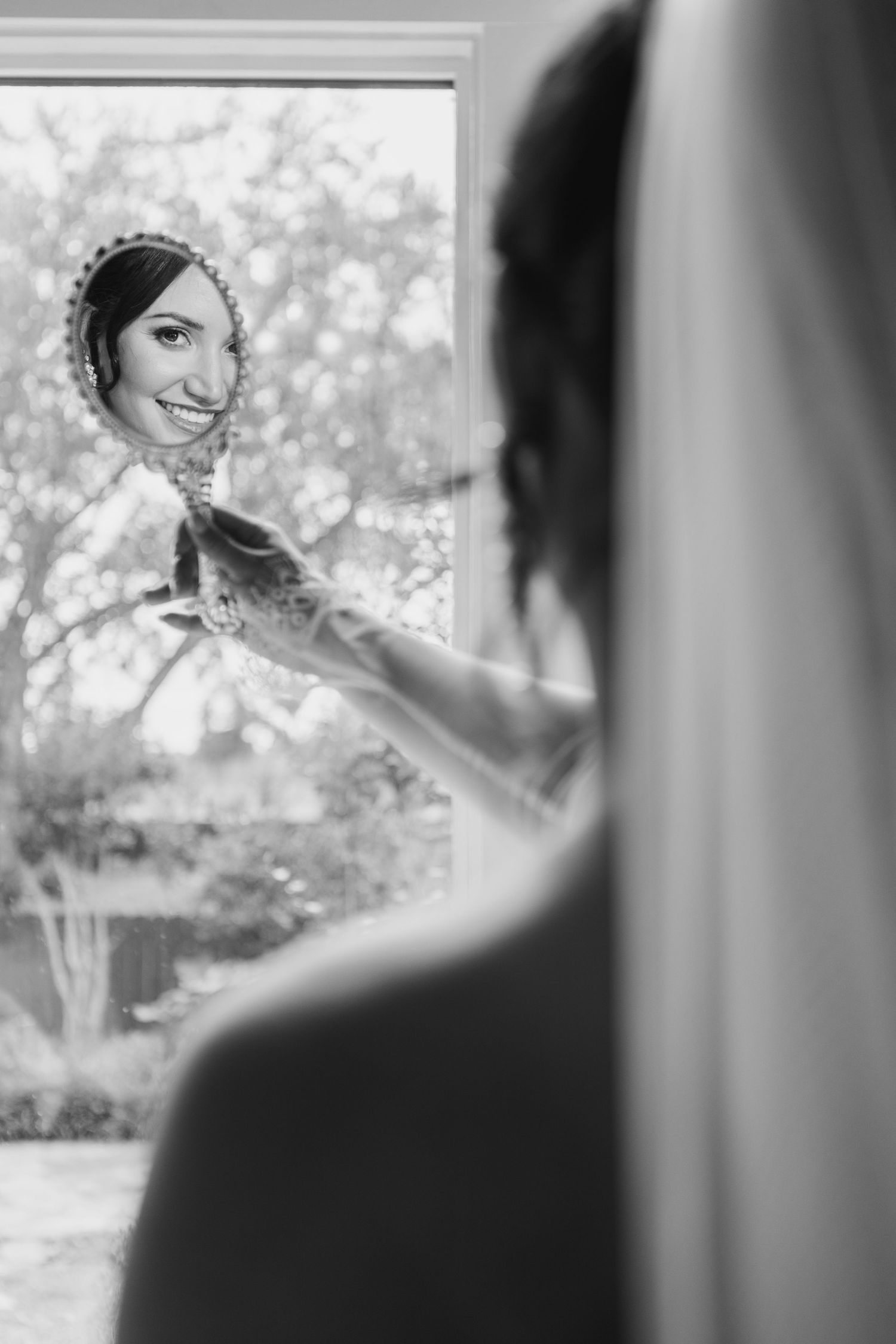Black and white reflection in mirror shows a bride getting ready on her wedding day, with soft bokeh background.
