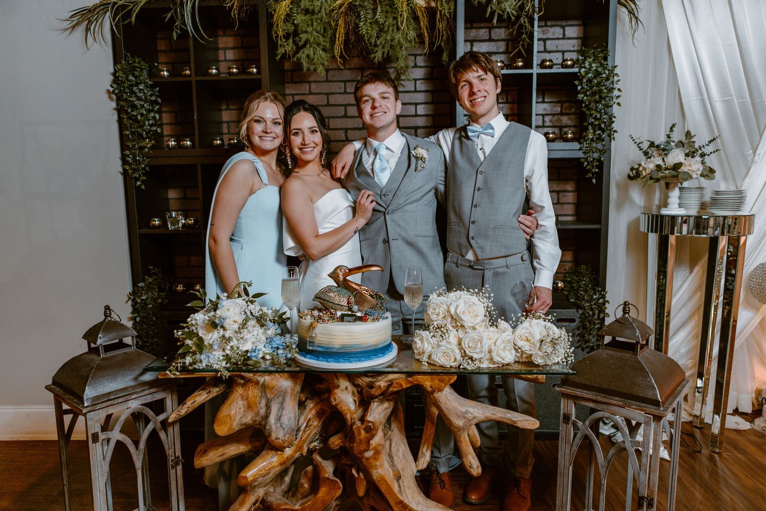 Wedding party poses behind elegant dessert table with rustic wooden base and metallic decorative elements.