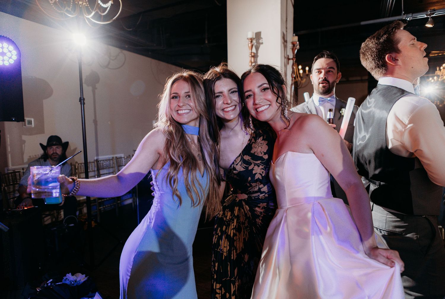Party guests dancing at a wedding reception with colorful purple lighting and festive atmosphere.