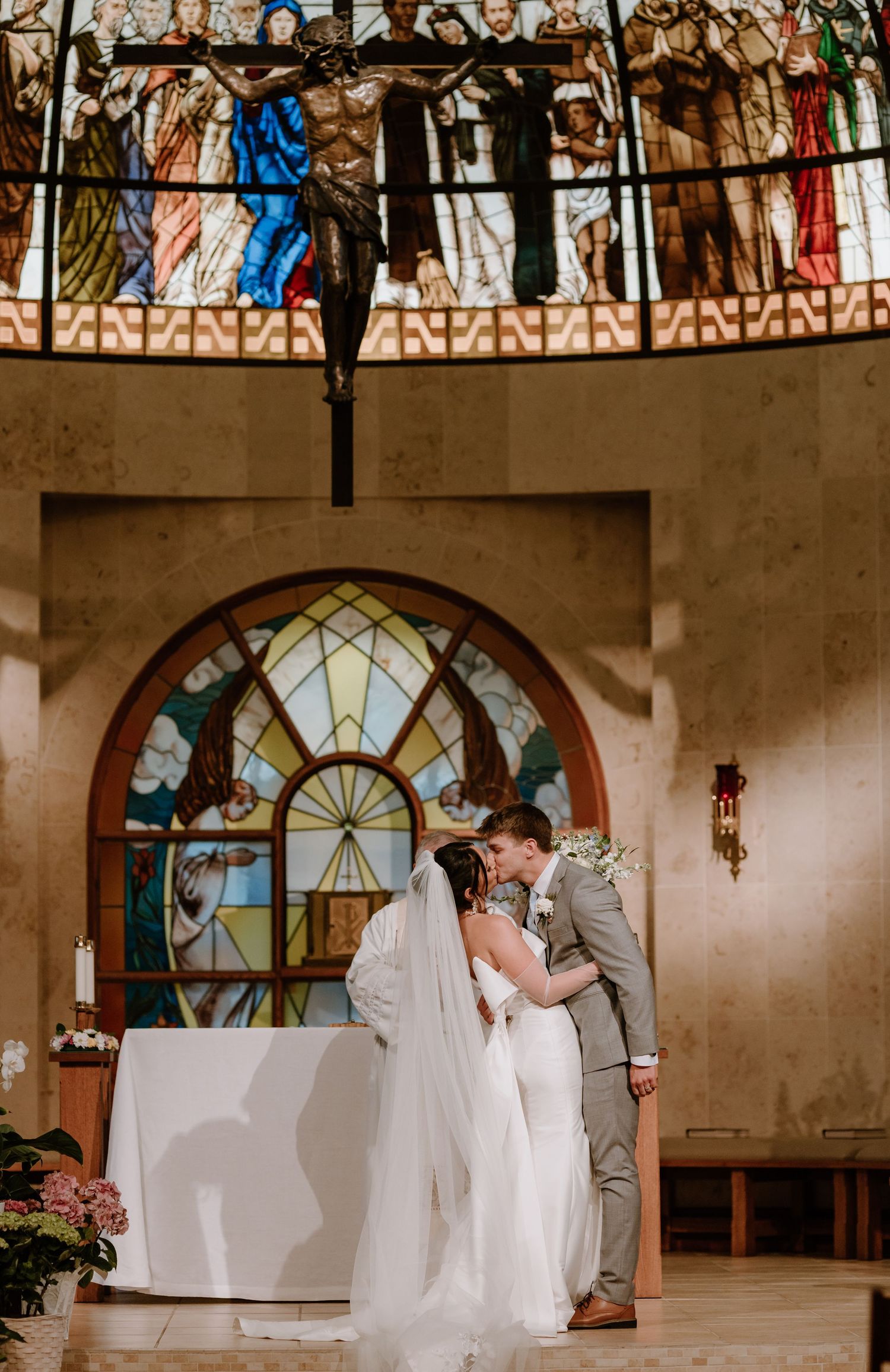 Beautiful church wedding ceremony with stained glass window and ornate architectural details in background.