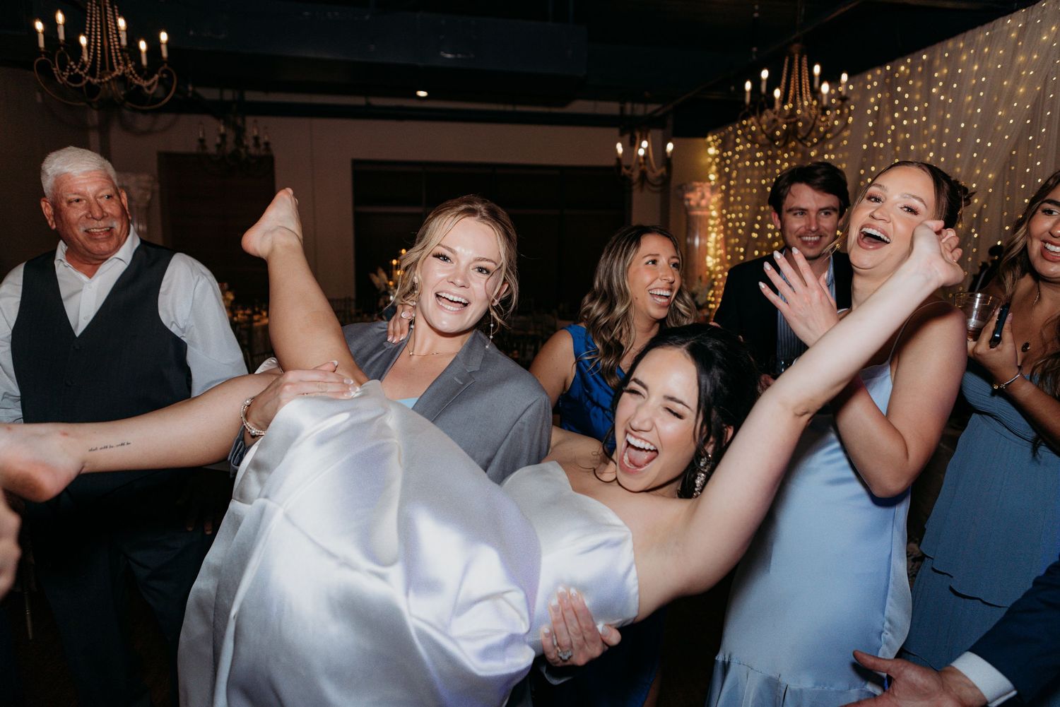 A joyful wedding reception with people dancing and celebrating under elegant lighting.