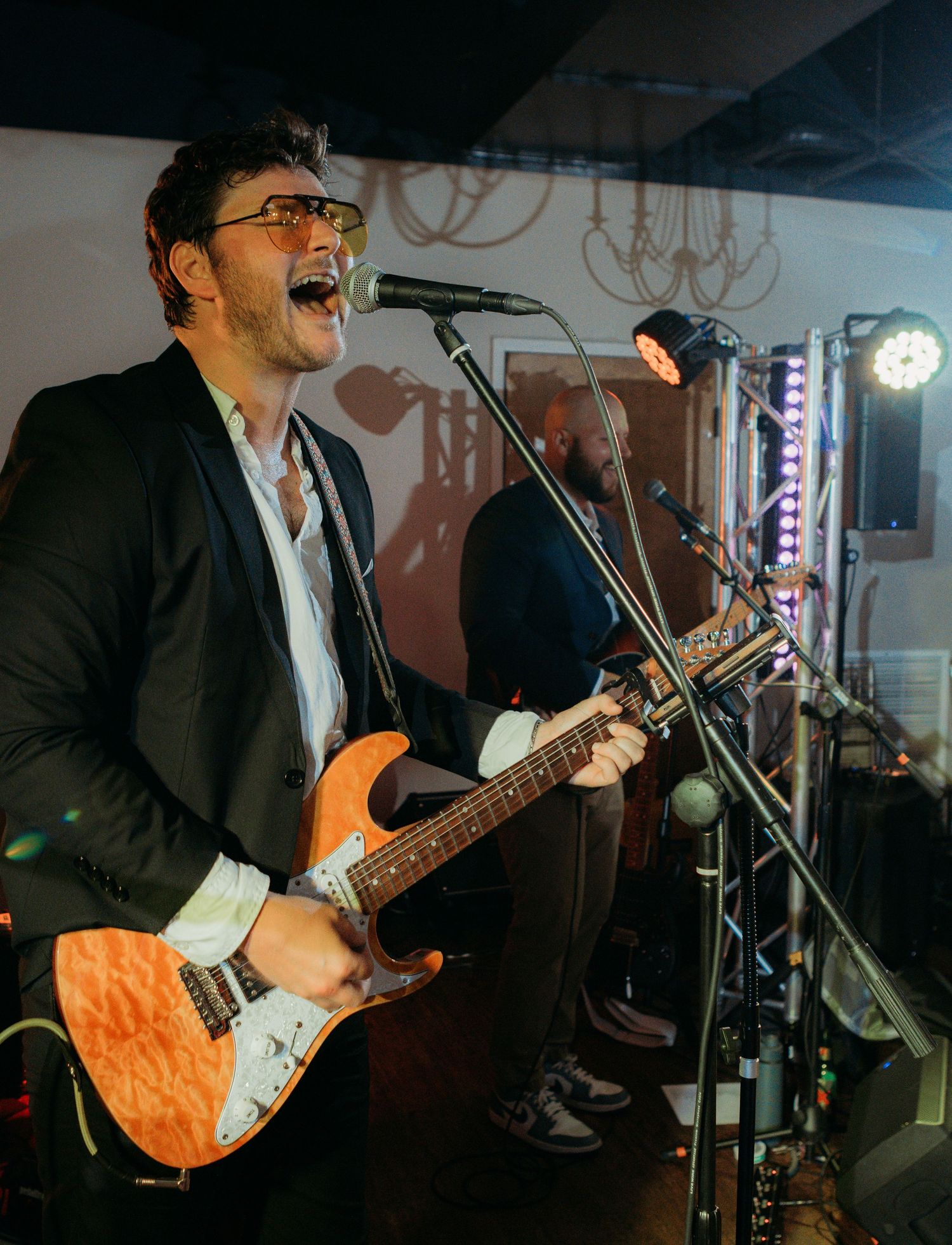Energetic musician performing with an orange electric guitar on stage under dramatic lighting.