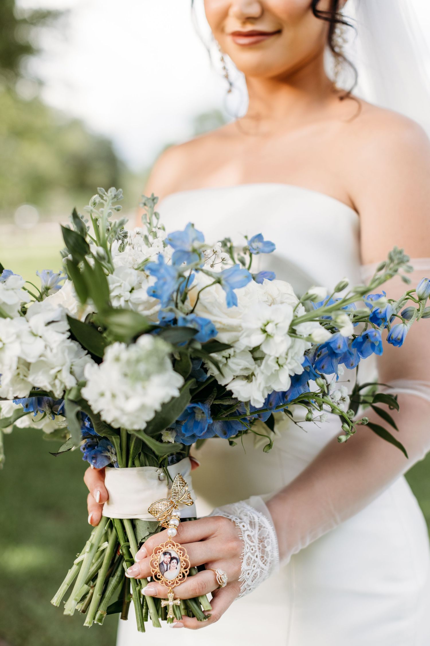Wedding bouquet with white and blue delphinium flowers held by bride in lace-detailed dress.
