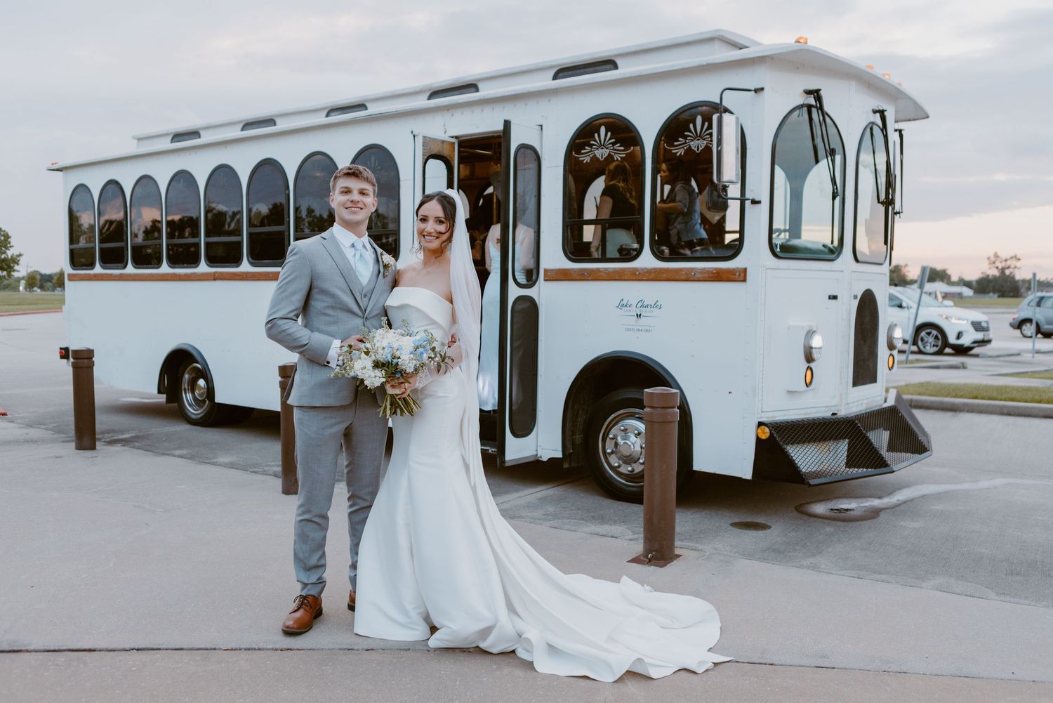A vintage white trolley bus serves as an elegant backdrop for a wedding ceremony in formal attire.