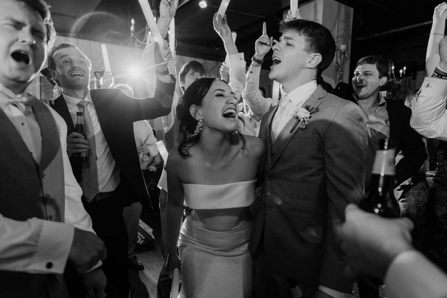 Joyful celebration captured in black and white as wedding guests dance and cheer at the reception.