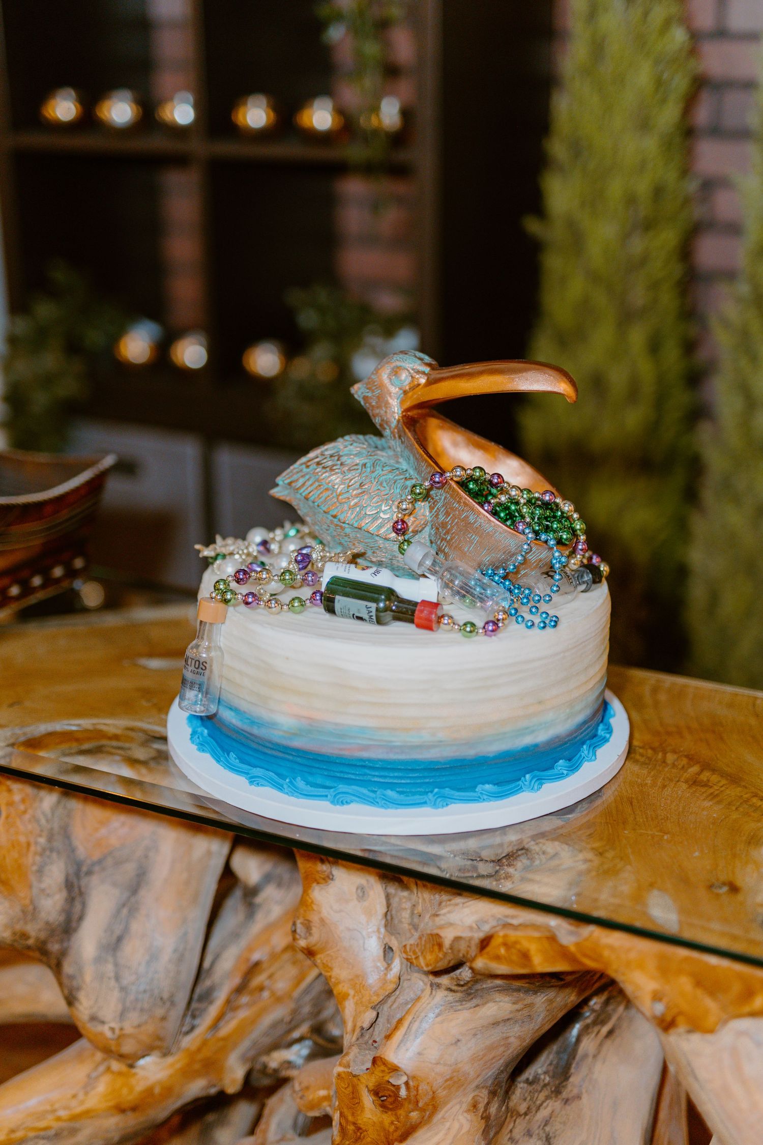 A whimsical ocean-themed cake with a silver pelican topper and blue waves on a rustic wooden table.