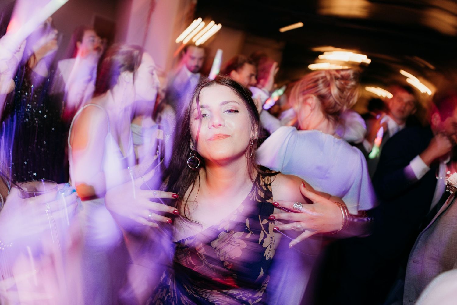People dancing and celebrating at a lively wedding reception with purple lighting effects.