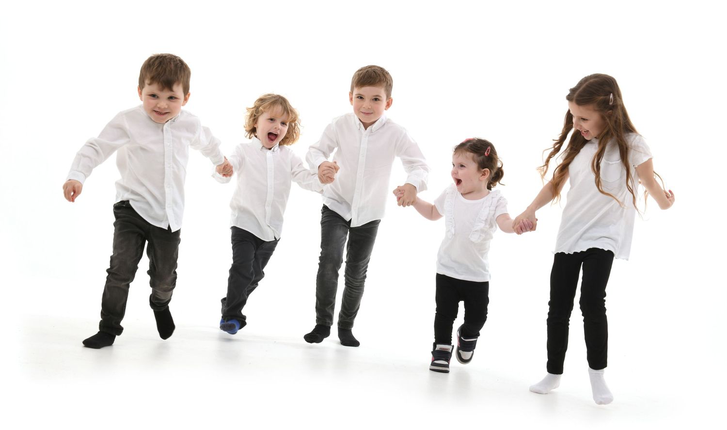 Five children in white tops and dark pants jump and dance together on a white background.