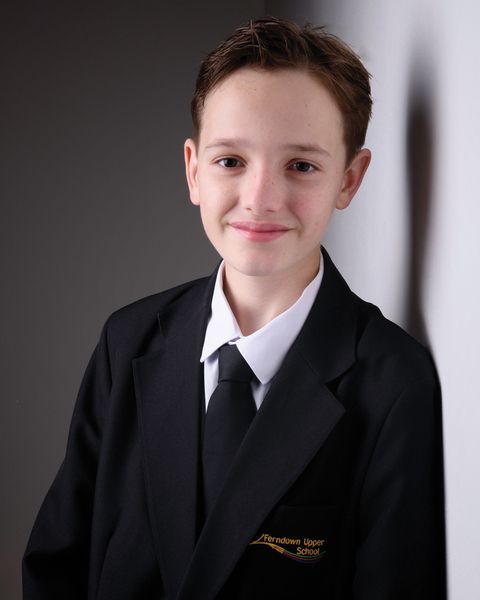 Young student in formal black suit and tie sitting for a professional school portrait photograph.