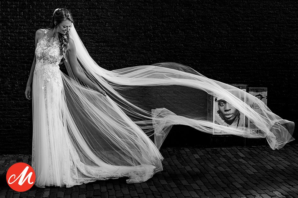 Black and white wedding photo showing flowing white veil dramatically sweeping across dark background.