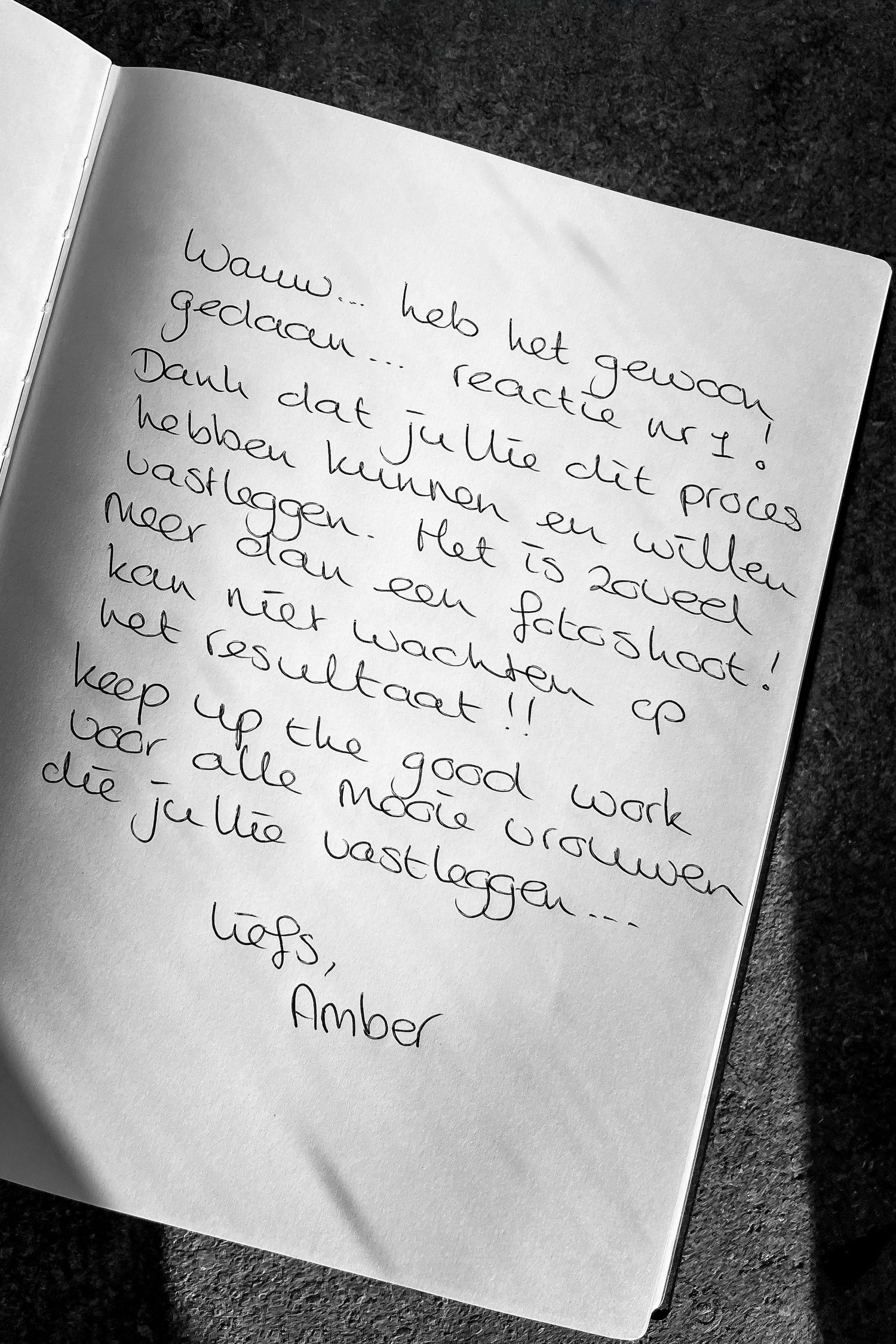 A handwritten note in black ink on a white paper page shown in black and white photography.