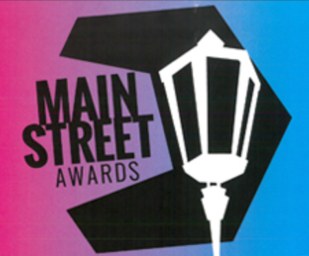 A stylized black and white logo featuring text 'Main Street Awards' with a decorative vintage street lamp design.