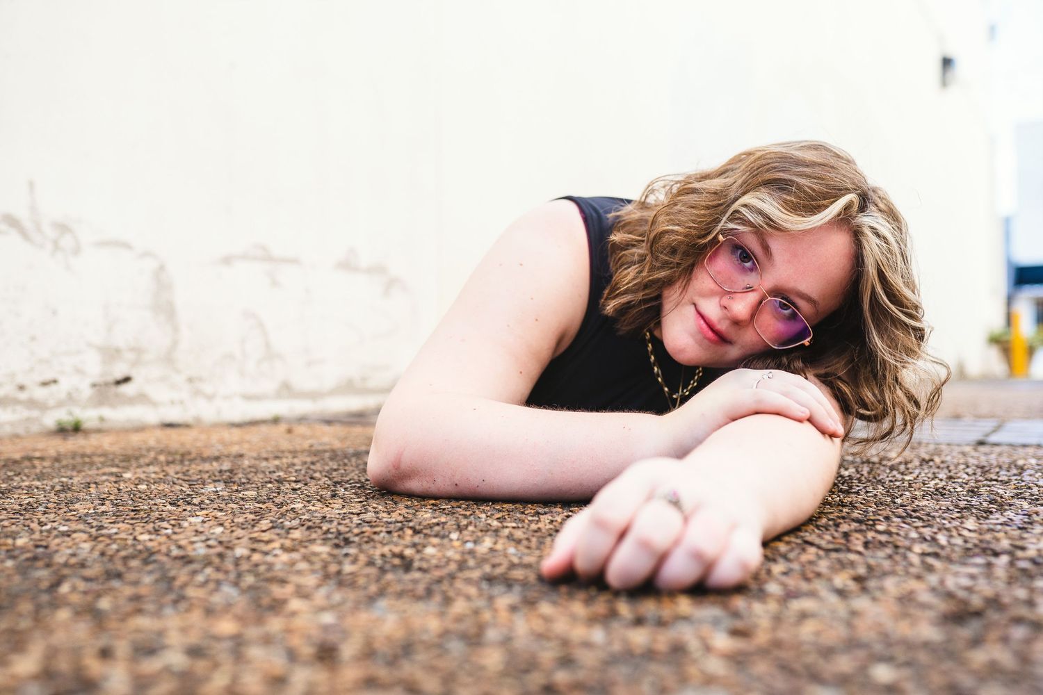 Someone in sunglasses lays on a rough ground surface with an outstretched arm.