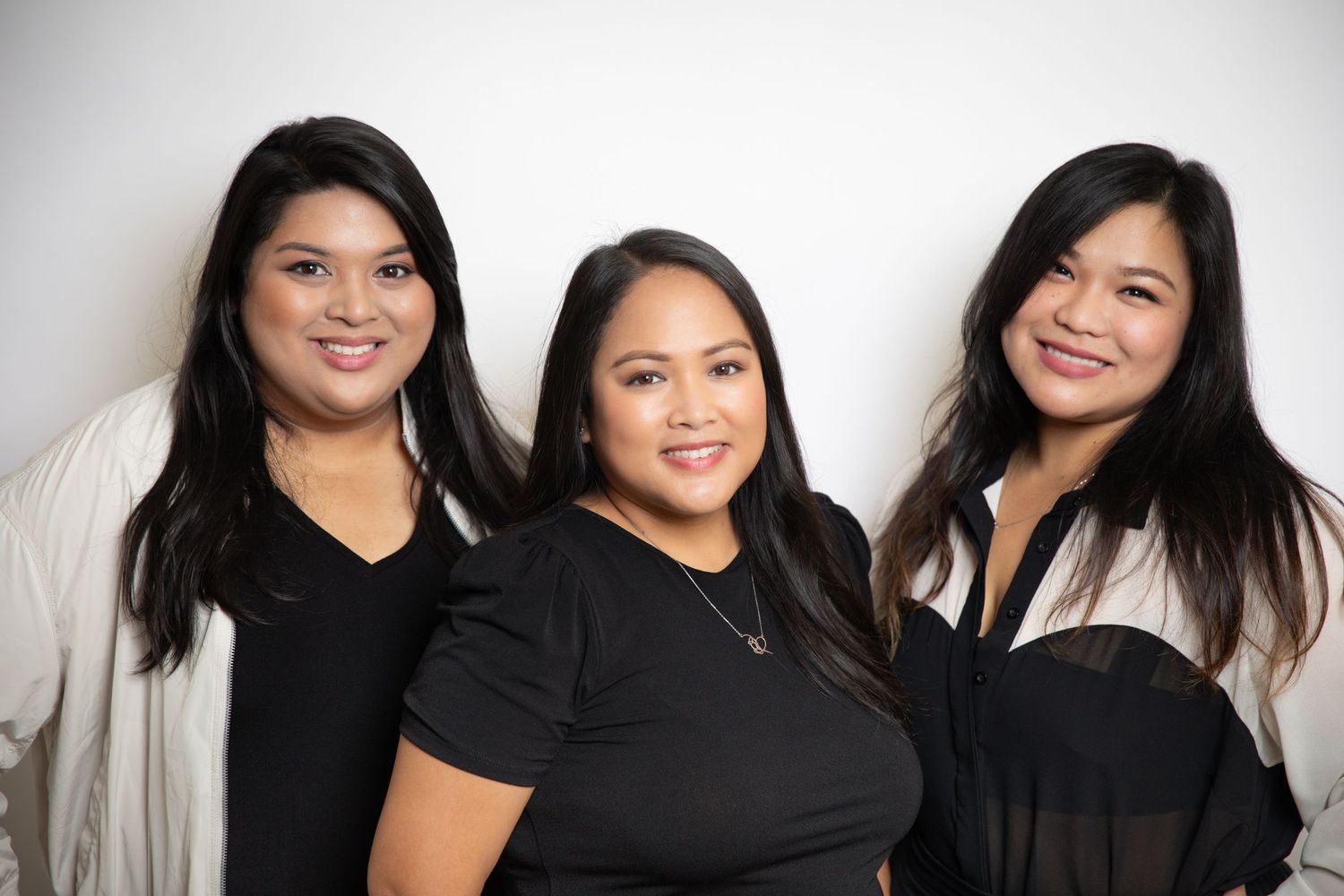 Studio portrait of three women in black outfits against white background.