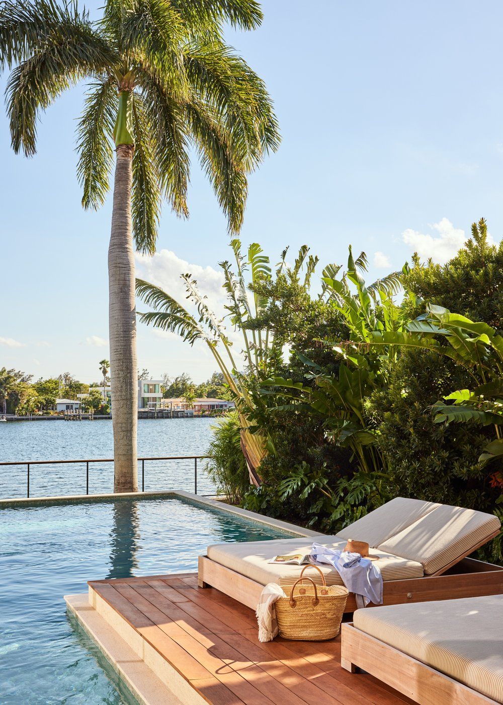 Luxurious poolside lounge chairs and palm trees overlook a serene waterfront view at a tropical resort.