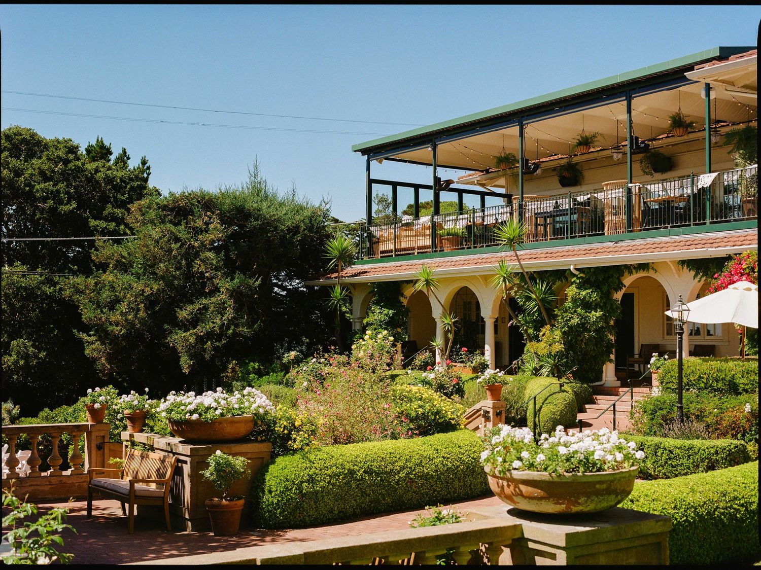Mediterranean-style restaurant terrace with arched colonnade and lush garden overlooking scenic hillside dining area.