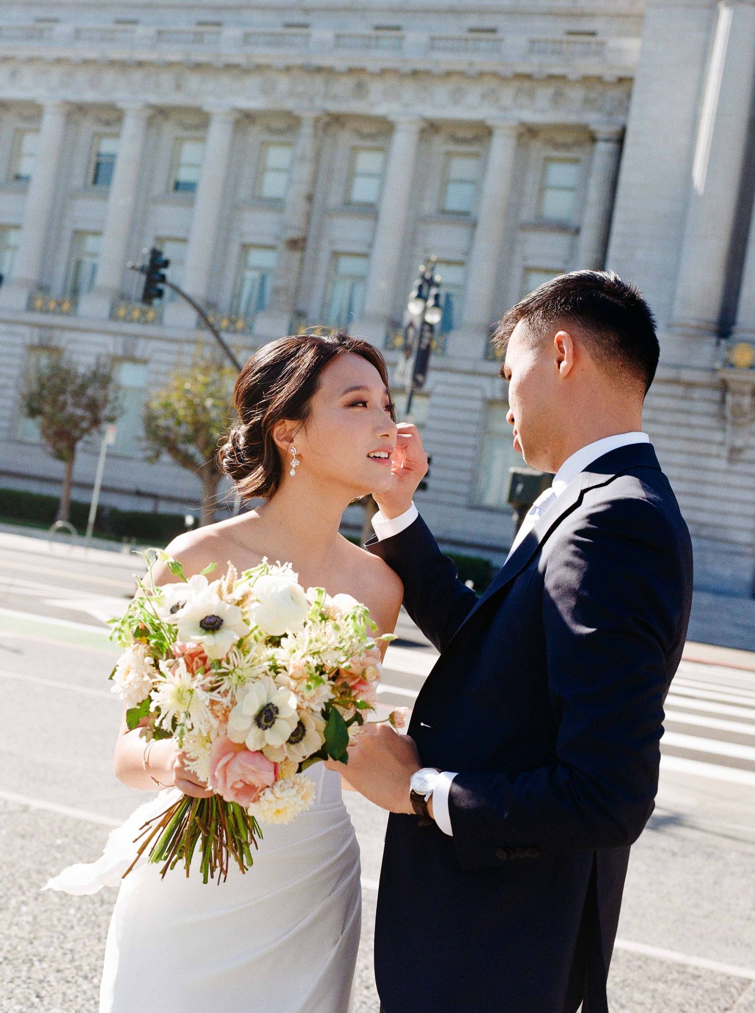A joyful wedding moment on the steps of a grand government building with a beautiful bouquet of white and pink flowers.