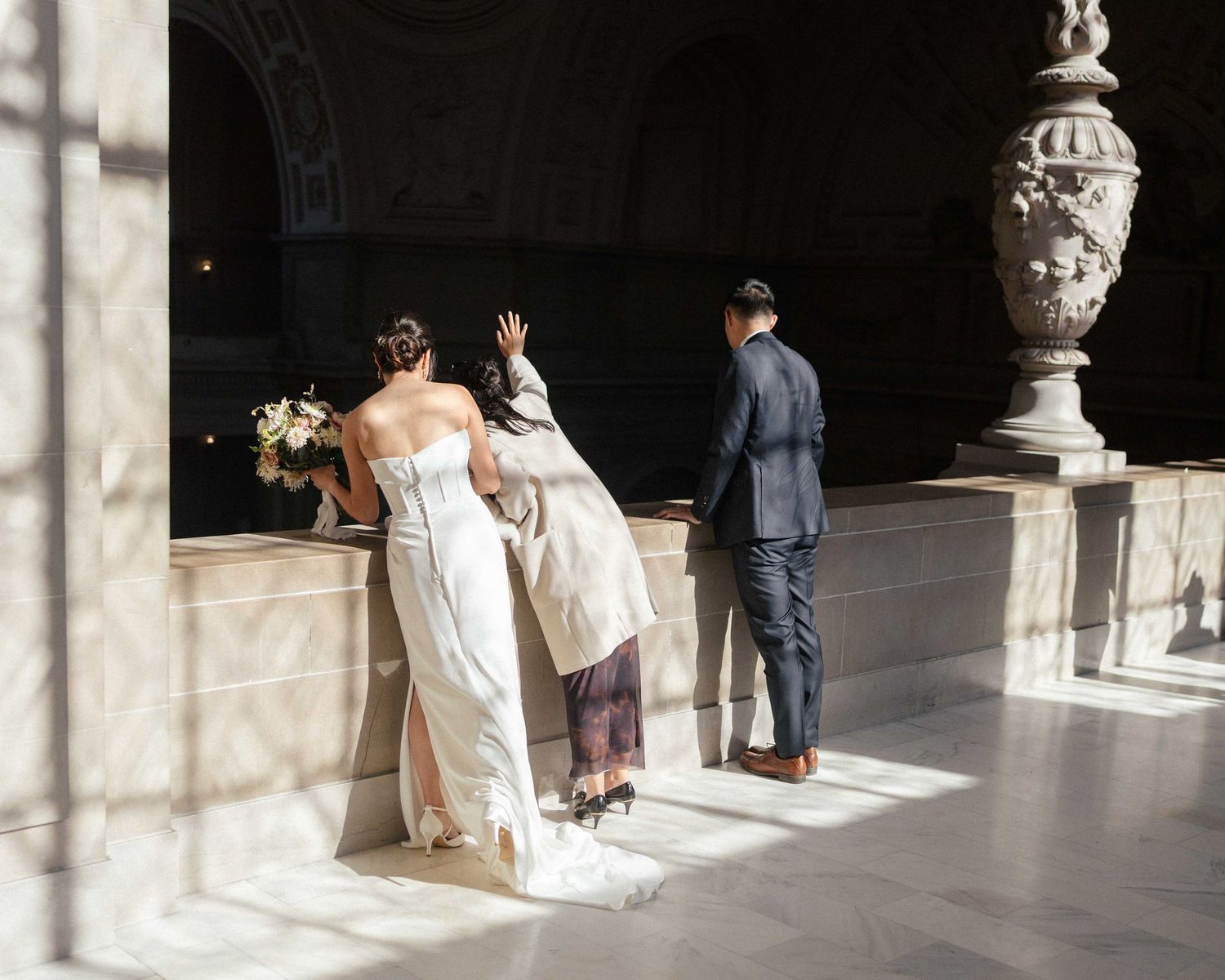 People in formal attire stand in an elegant hallway with ornate stone architecture and decorative urns.