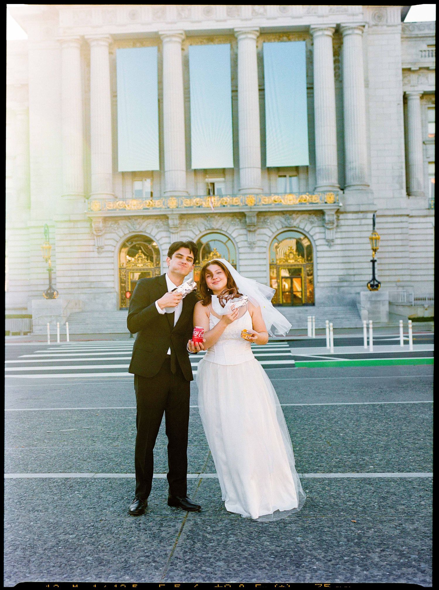 A bride and groom pose playfully in front of a grand classical building with white columns at dusk.