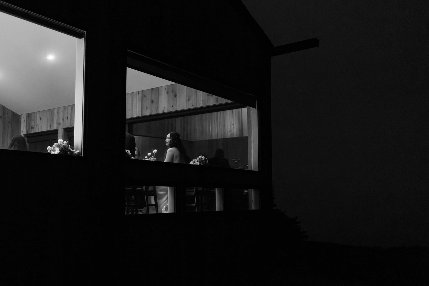 A dimly lit room with a window showing silhouettes and glowing objects on shelves in black and white.