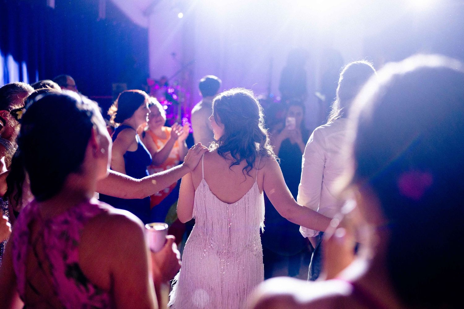People dancing together at a wedding reception with purple lighting and a festive atmosphere.