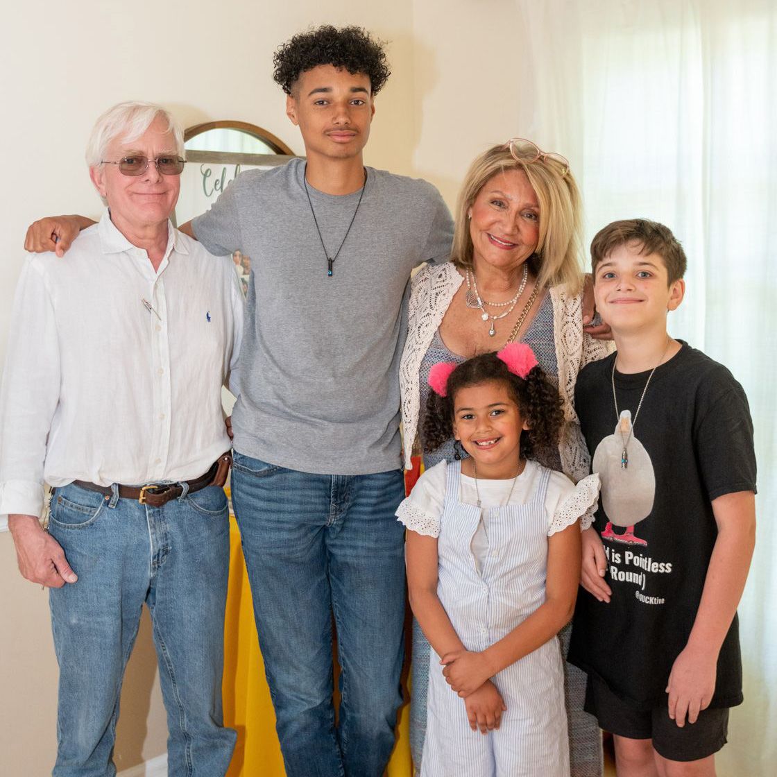 Multi-generational family poses together in casual attire against a light wall.