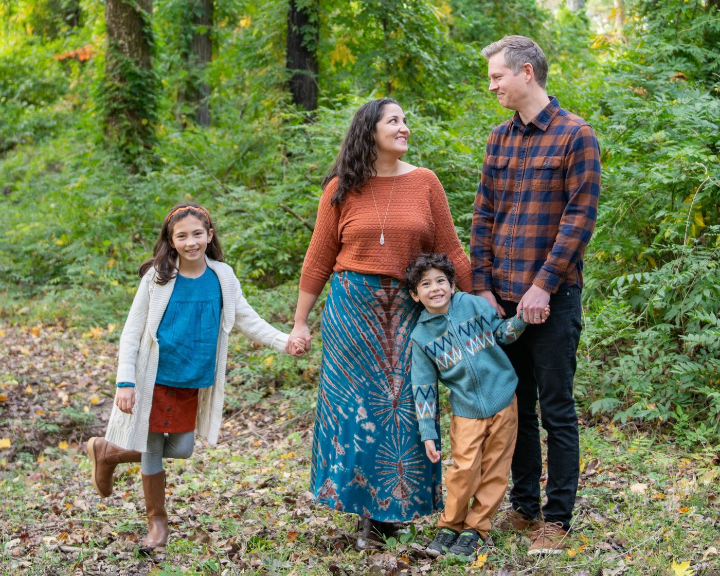 Family walking together through a lush green forest setting wearing casual autumn clothing.