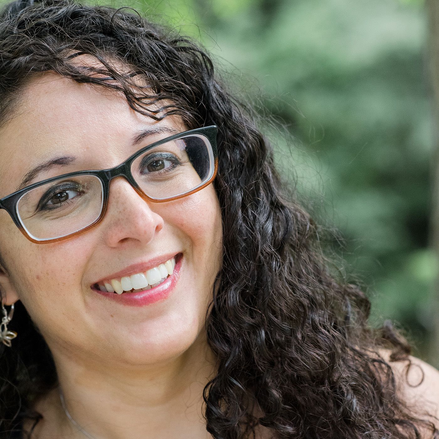Portrait of person with curly dark hair and glasses against green background.