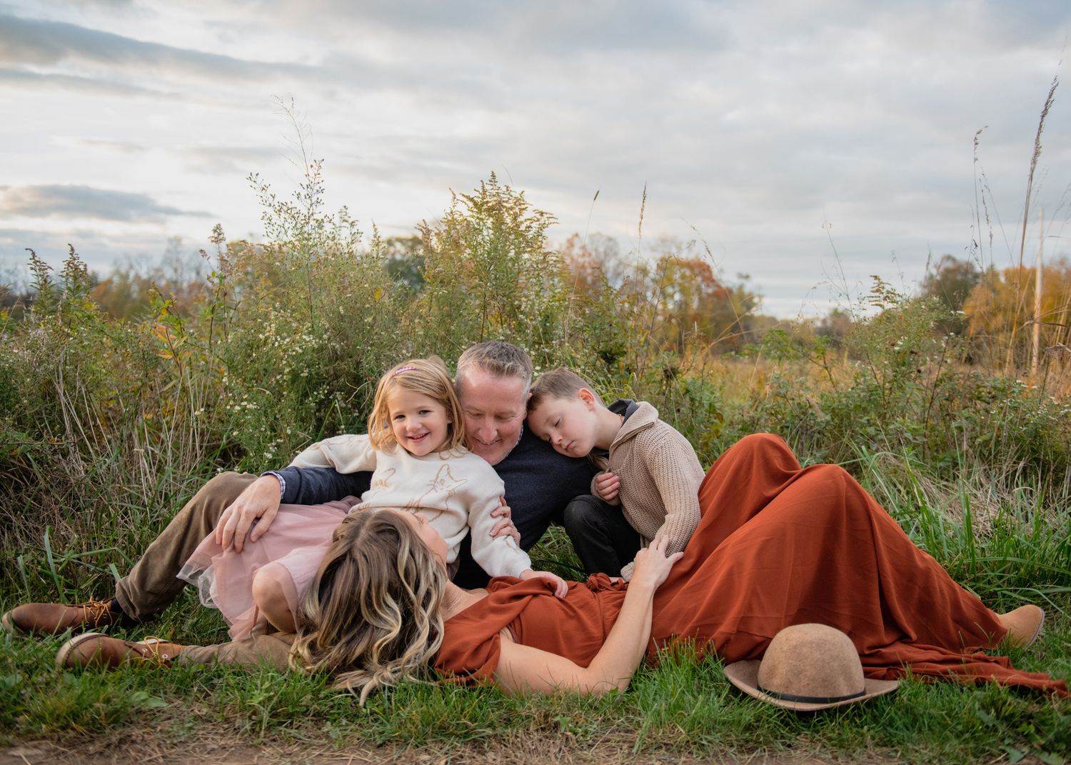Family snuggling together on blankets outdoors with natural autumn foliage in background.