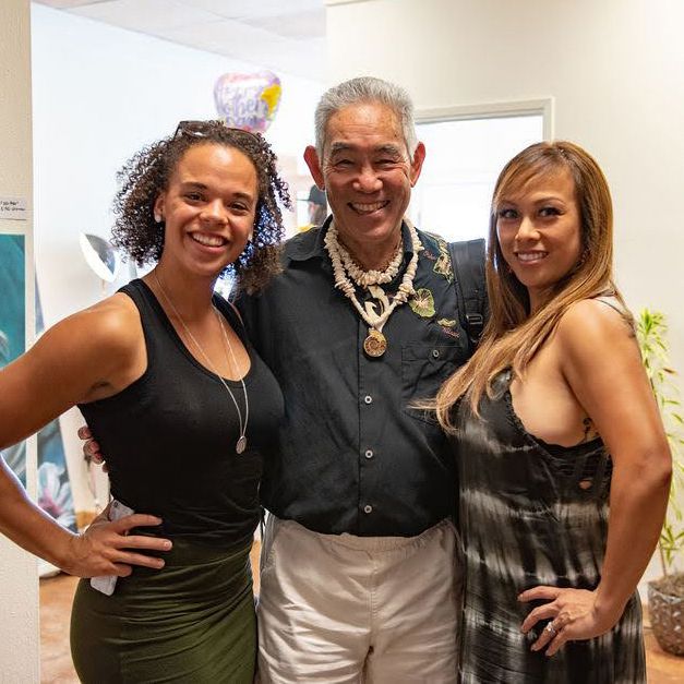 Three people pose at cultural event wearing formal attire and traditional accessories.